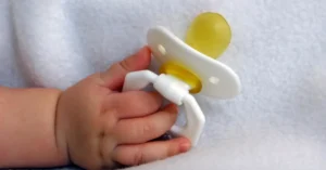 Bebeğin elinde tuttuğu sarı uçlu emzik, beyaz battaniye üzerinde (temsili görsel)